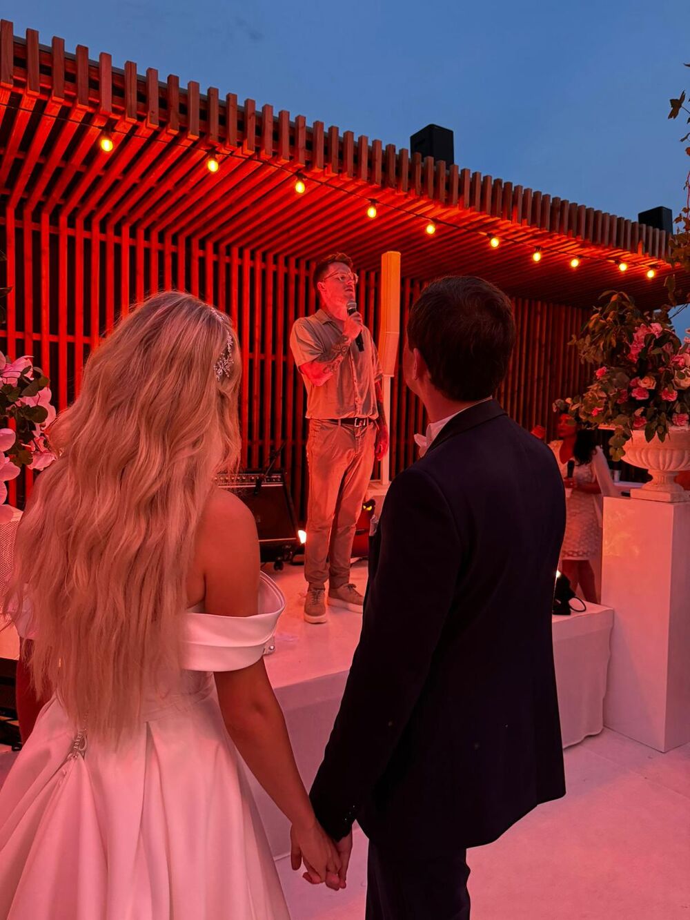 A bride and groom holding hands as Nathan Grisdale performs for them